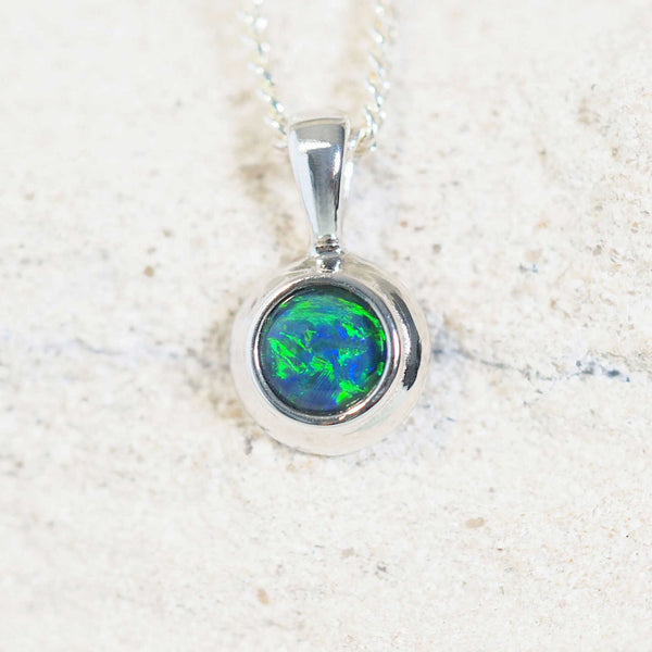 a close up of a blue and green opal pendant set in silver