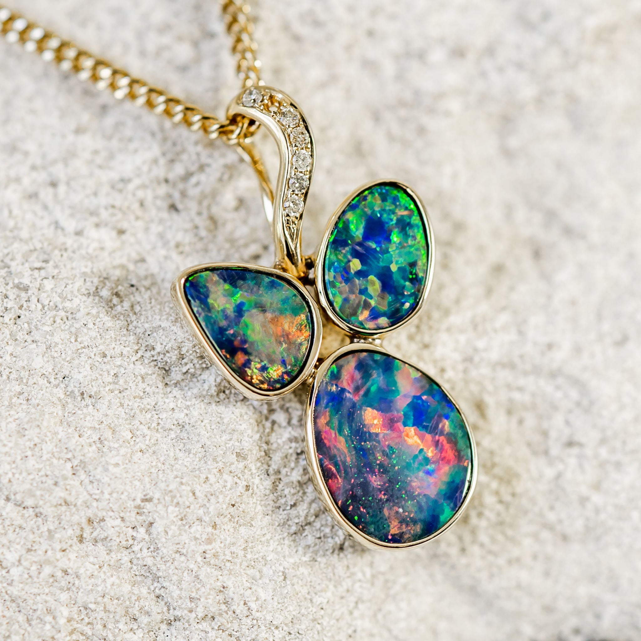 A stunning custom-designed 14ct yellow gold necklace pendant bezel set with three vibrant multi-coloured Australian doublet opals and seven diamonds.