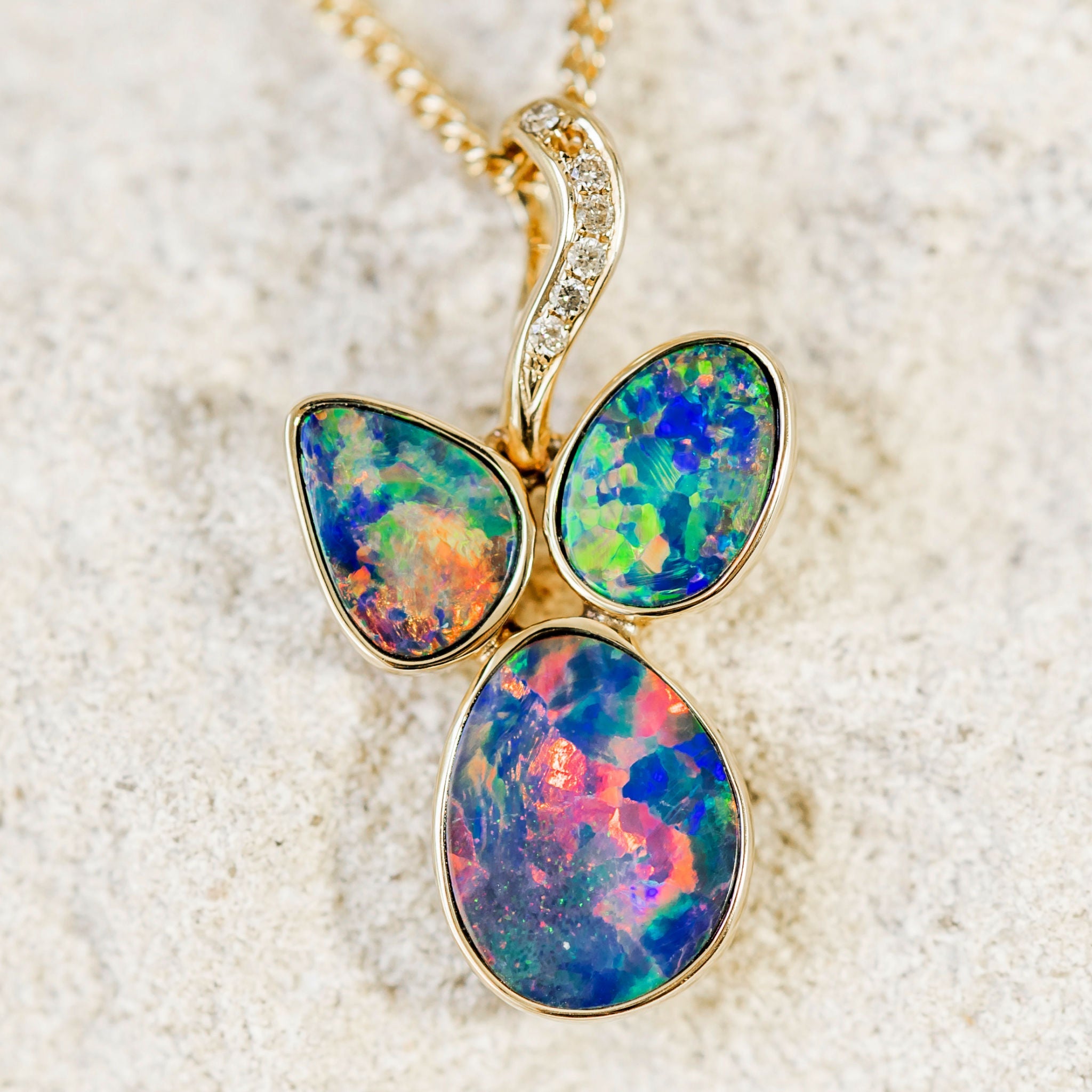 A stunning custom-designed 14ct yellow gold necklace pendant bezel set with three vibrant multi-coloured Australian doublet opals and seven diamonds.