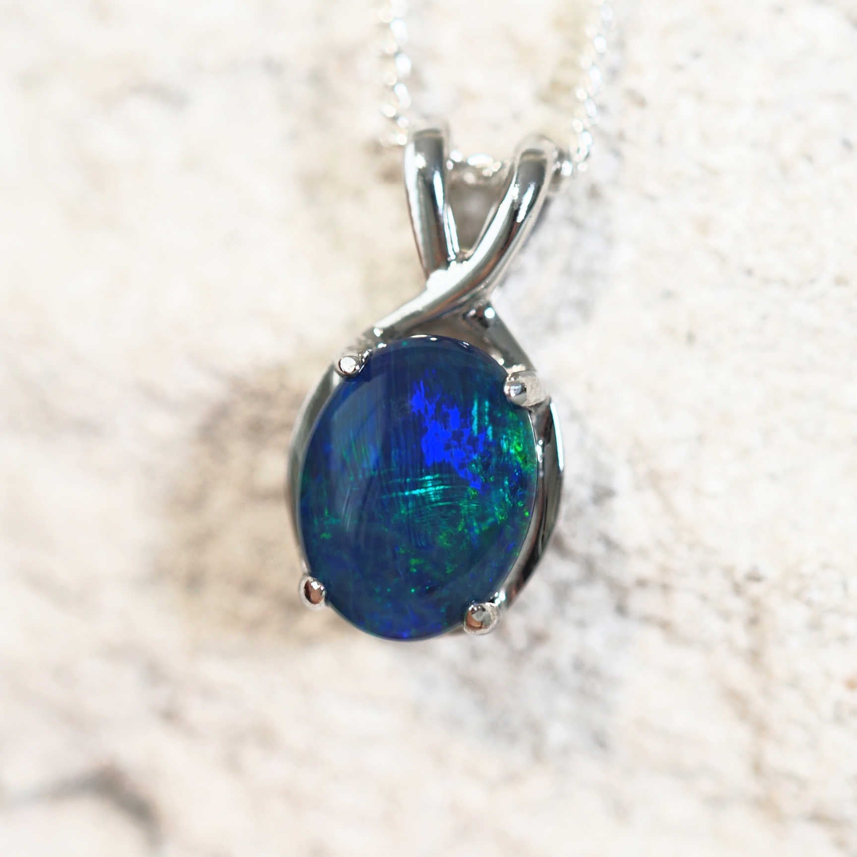 close up of an opal pendant featuring a blue and green triplet opal stone in silver