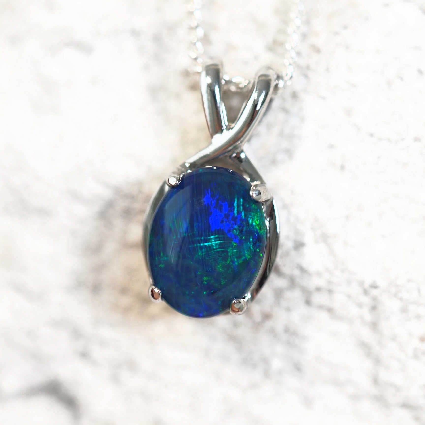 close up of an opal pendant featuring a blue and green triplet opal stone in silver