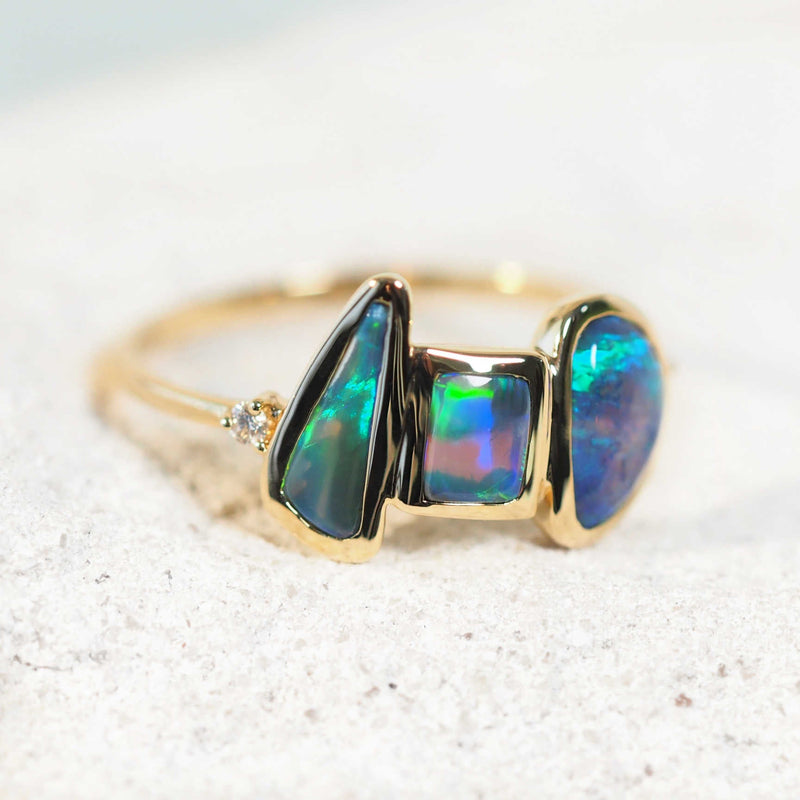 three black opals set into a gold ring with two accent diamonds