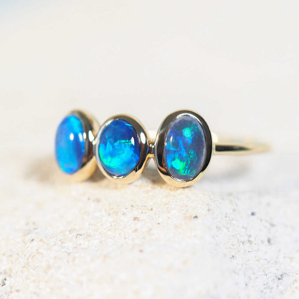 three green and blue opals in a gold ring